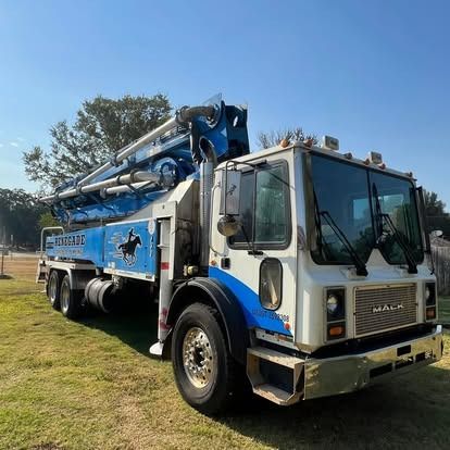 A white and blue concrete pump truck is parked in a grassy field.
