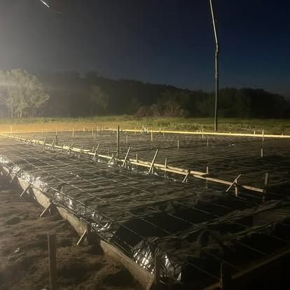 A concrete slab is being poured at night in a field.