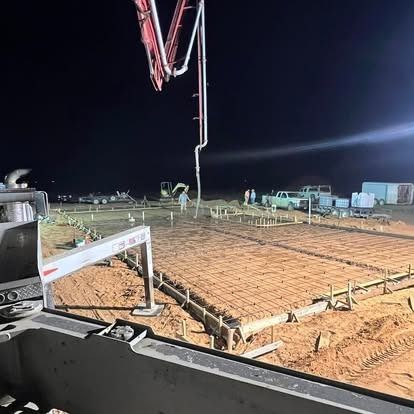 A concrete pump is being used to pour concrete on a construction site at night.