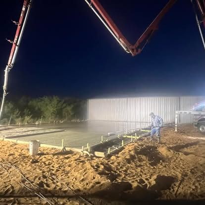 A man is pouring concrete on a construction site at night.