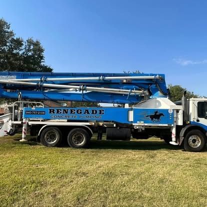 A renegade concrete pump truck is parked in a grassy field.