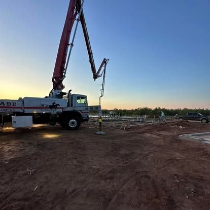 A concrete pump truck is working on a construction site at sunset.