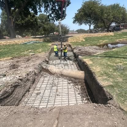 Two construction workers are working on a concrete walkway in a park.