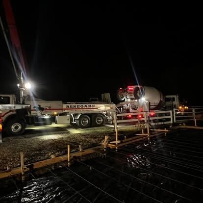 A concrete pump truck is pouring concrete into a concrete slab at night.