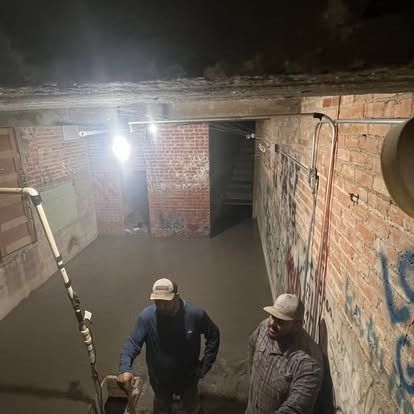 Two men are standing in a dark room with a brick wall.