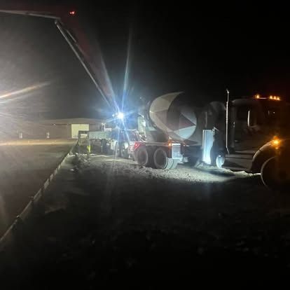 A concrete mixer truck is driving down a road at night.