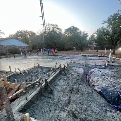 A group of people are working on a concrete base for a house.