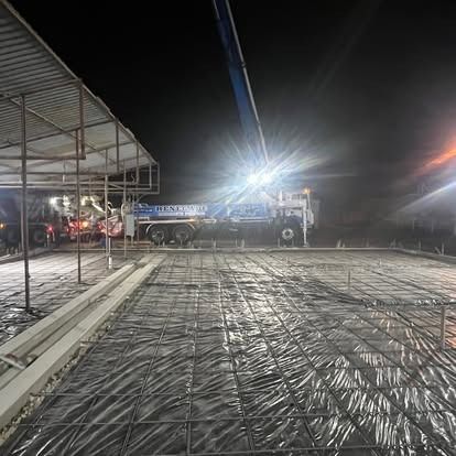 A concrete pump is pouring concrete into a concrete slab at night.