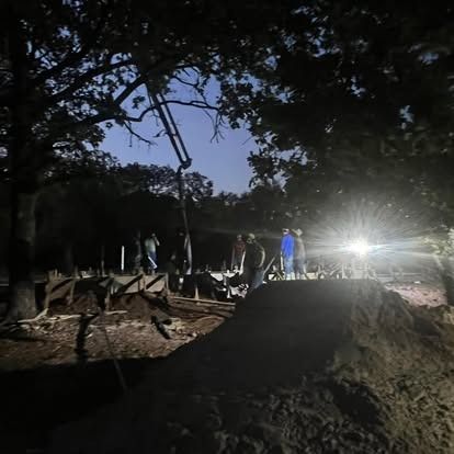 A group of people are standing on top of a dirt hill at night.
