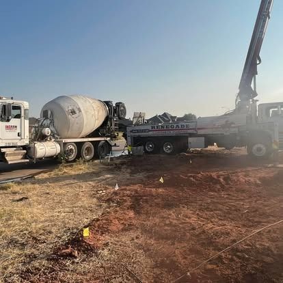 A concrete mixer truck is driving down a dirt road next to a crane.