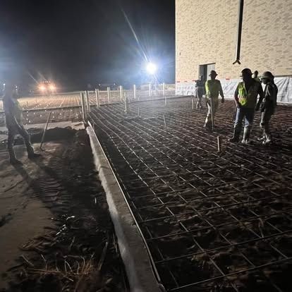 A group of construction workers are working on a concrete floor at night.