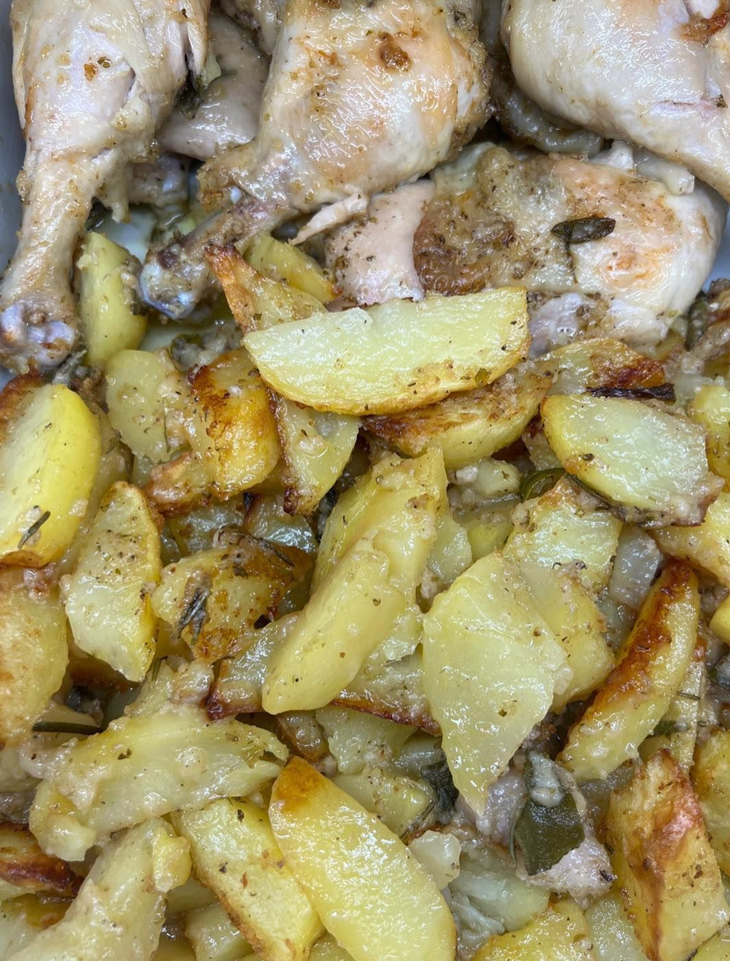 Pollo arrosto e patate in una teglia. Le patate sono dorate e il pollo è dorato.