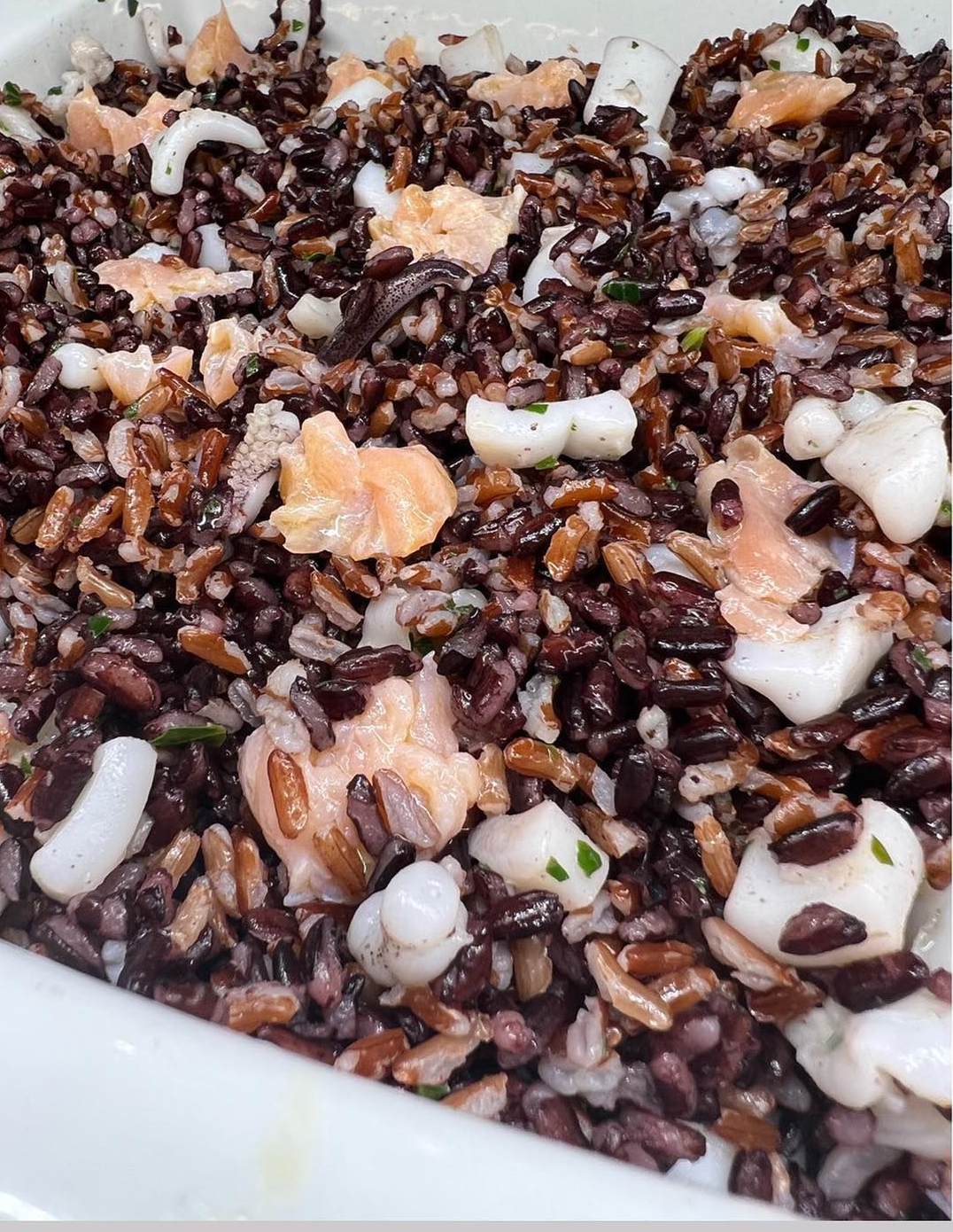 Insalata di riso nero con salmone e calamari in un piatto bianco.