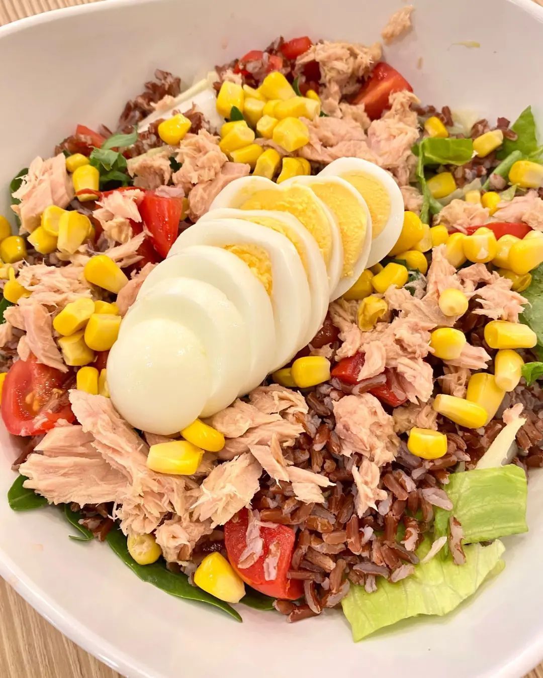 Insalata di tonno con mais, pomodori, riso e uova sode a fette in una ciotola bianca.