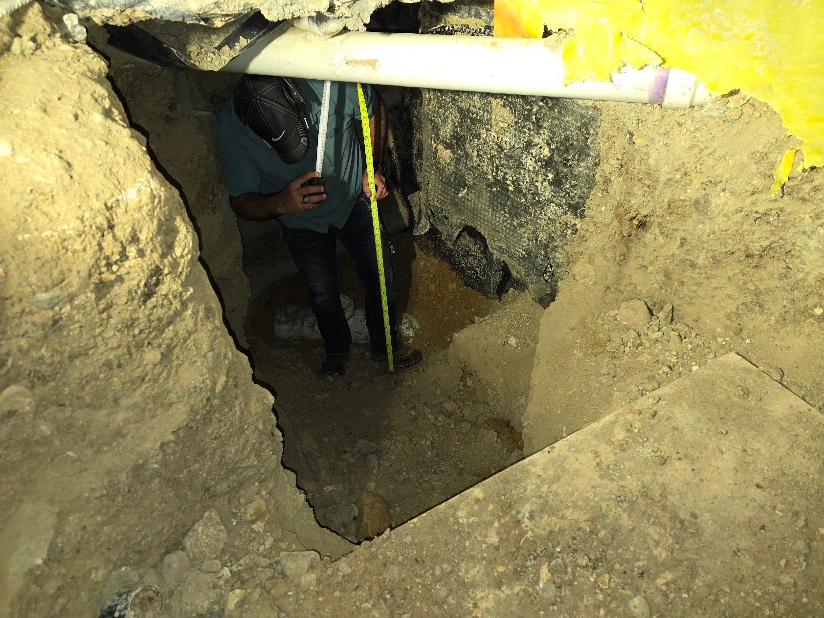 A man is measuring a hole in the ground with a tape measure