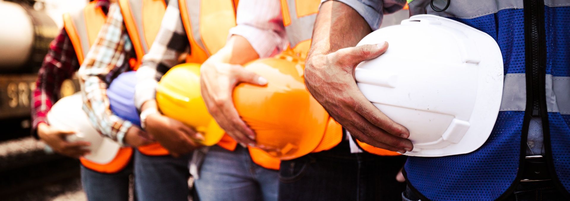 A group of construction workers are standing in a row holding hard hats.