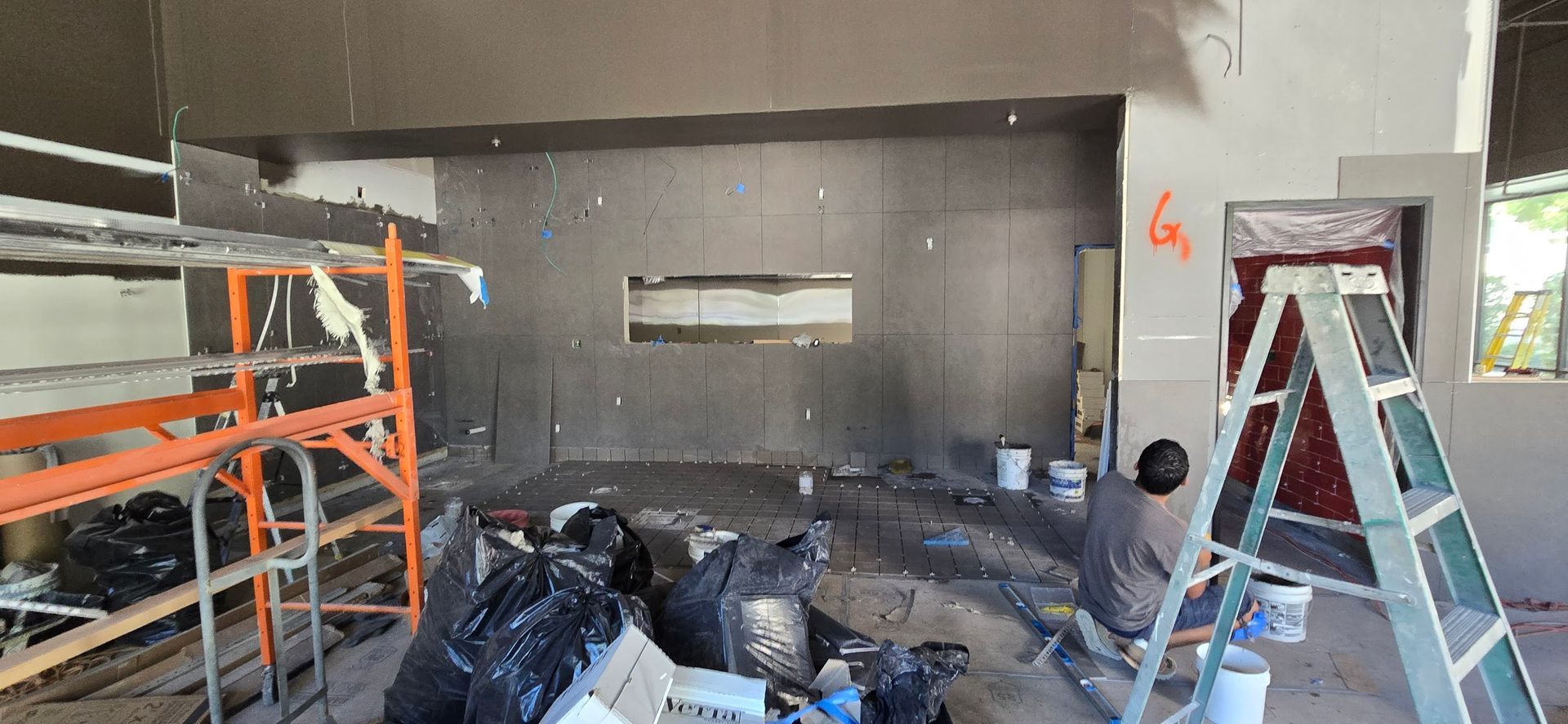 A man is standing on a ladder in a room under construction.