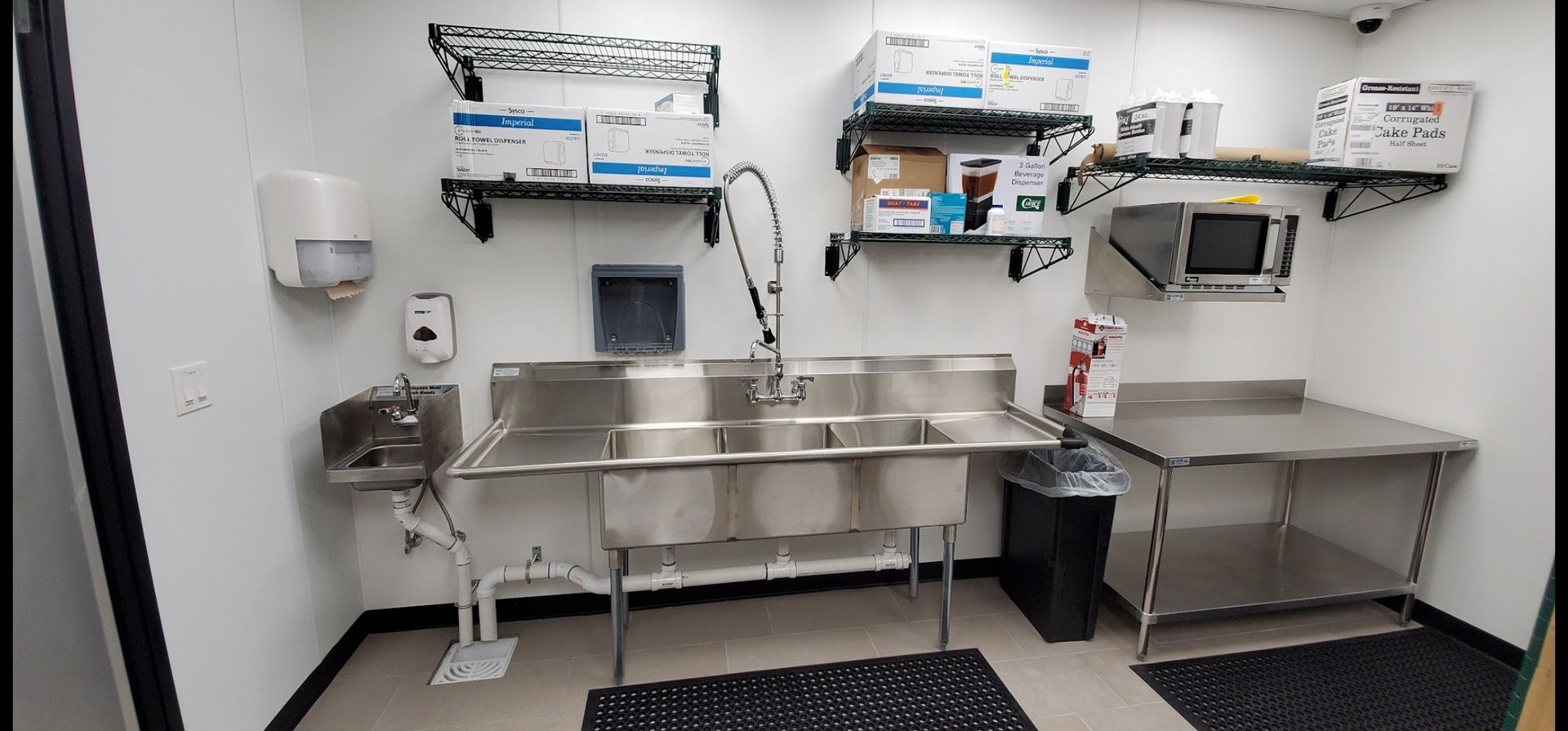 A kitchen with stainless steel sinks , tables , shelves and a microwave.