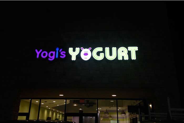 A sign for yogi 's yogurt is lit up at night