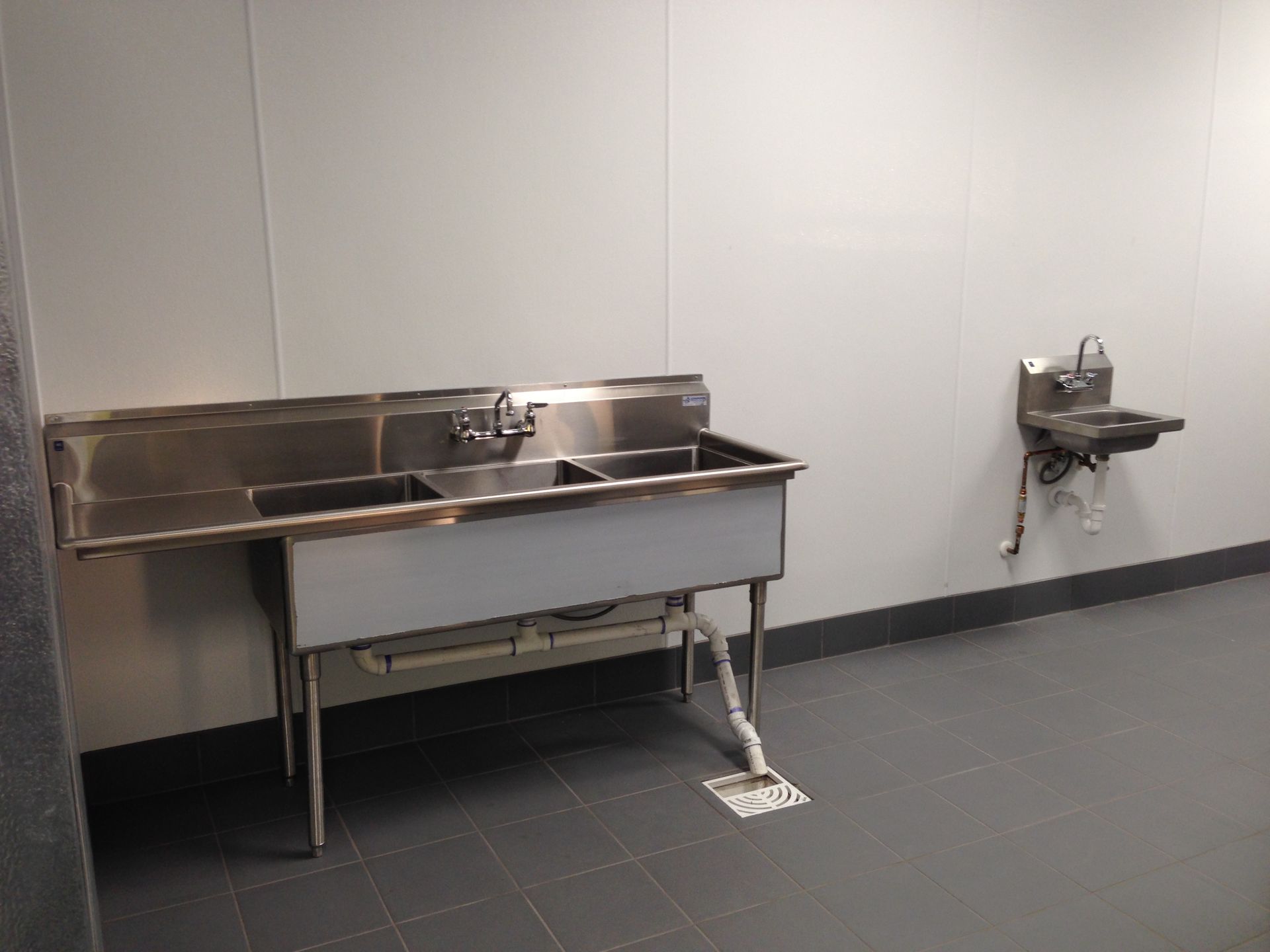 Two stainless steel sinks are in a room next to each other.