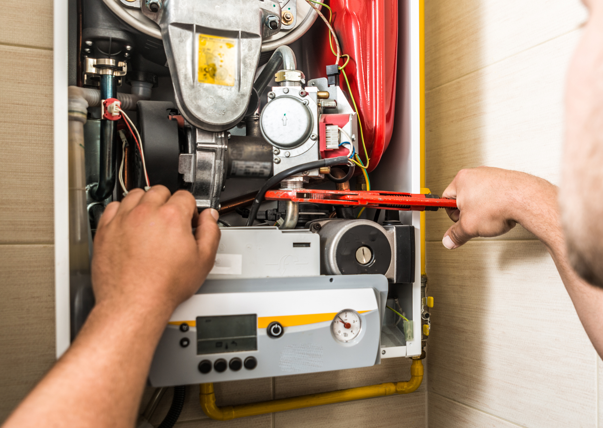 A man is fixing a boiler with a wrench.
