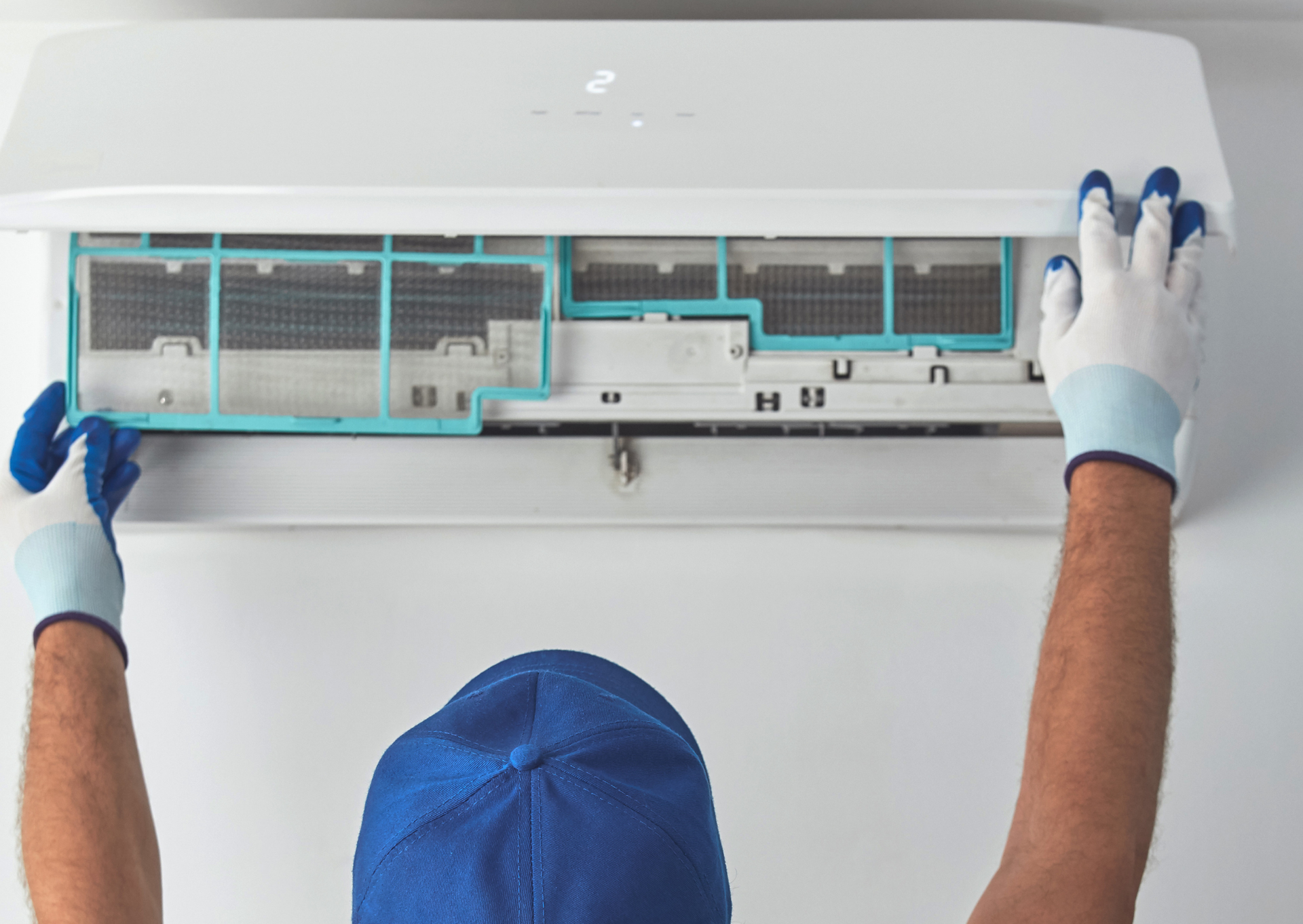 A man in a blue hat and gloves is cleaning an air conditioner.