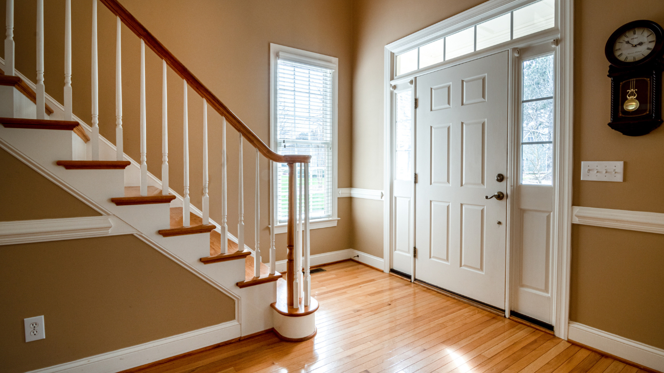 A hallway with stairs leading up to a door and a clock on the wall.