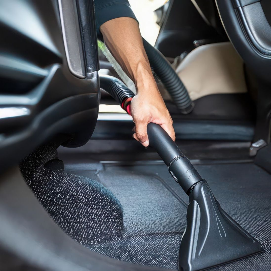 hand holding end of vacuum cleaning the back seat of a car