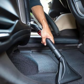 hand holding end of vacuum cleaning the back seat of a car