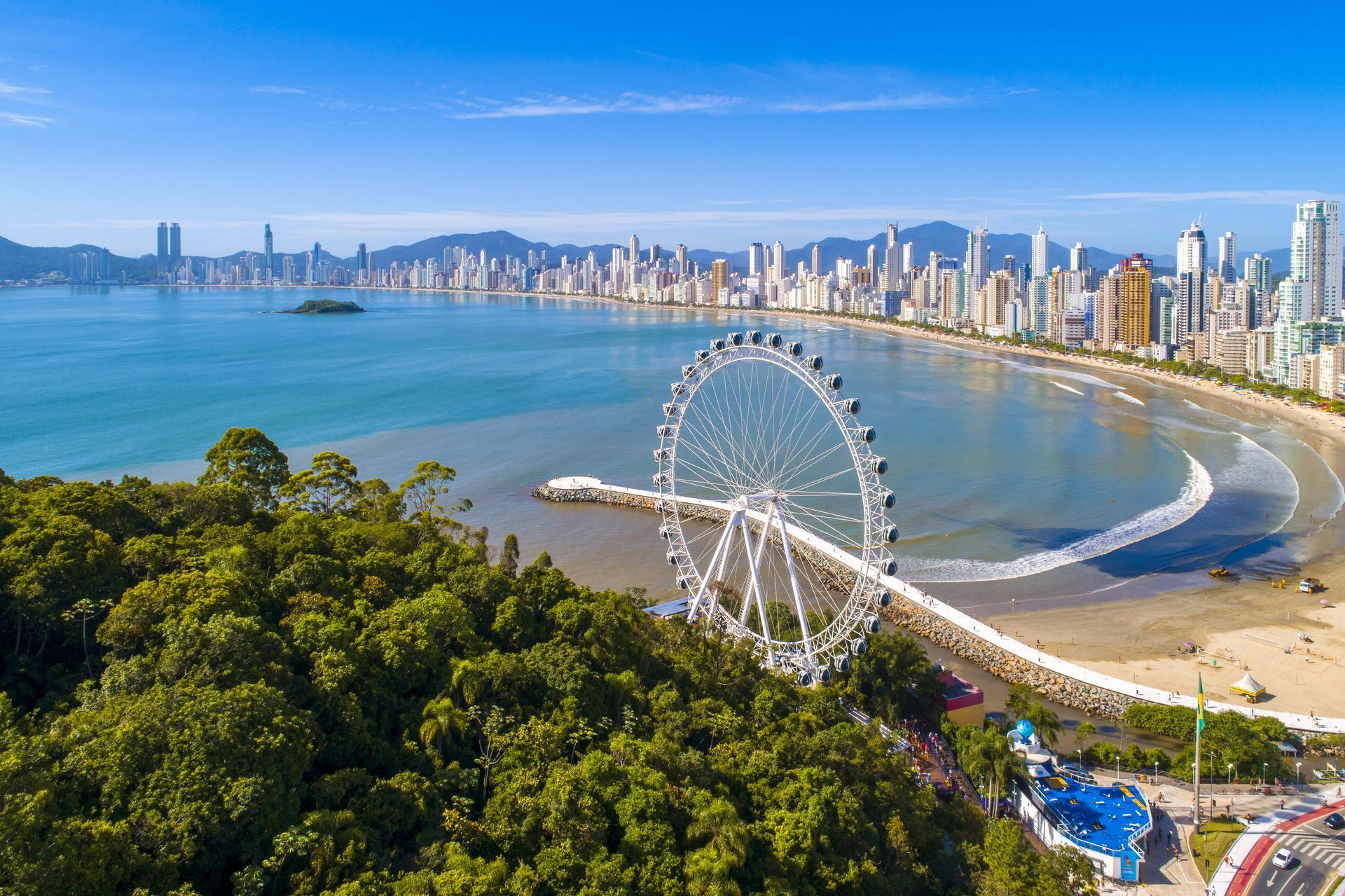 Vista aérea da roda gigante no molhe da Barra Norte, com mar calmo, orla em curva e skyline de BC