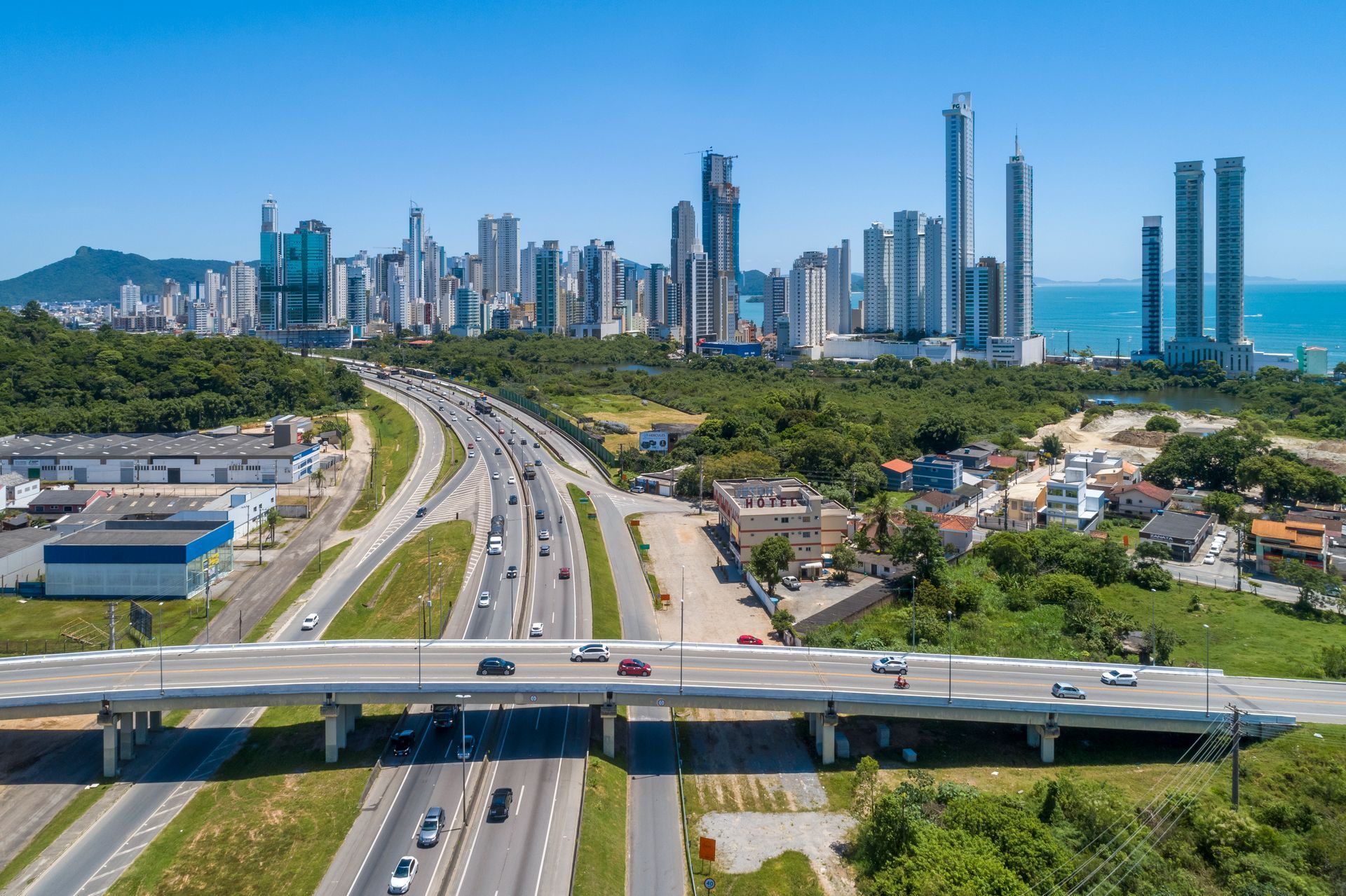 Vista aérea de rodovia com Balneário Camboriú ao fundo, entre prédios altos e o mar