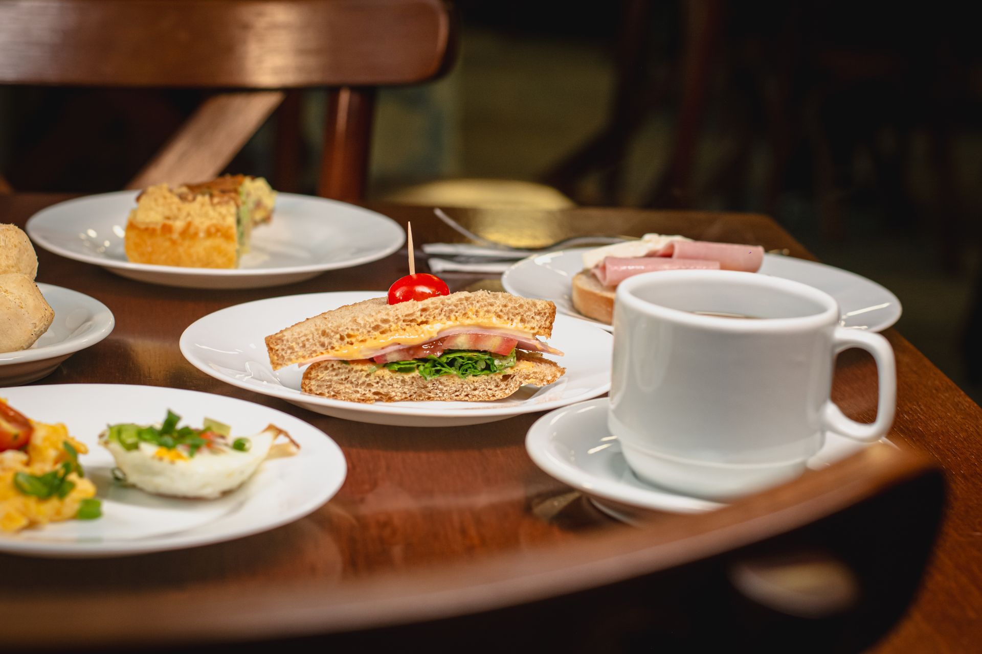 Mesa de café com sanduíches, ovos, bolo e xícara de café.