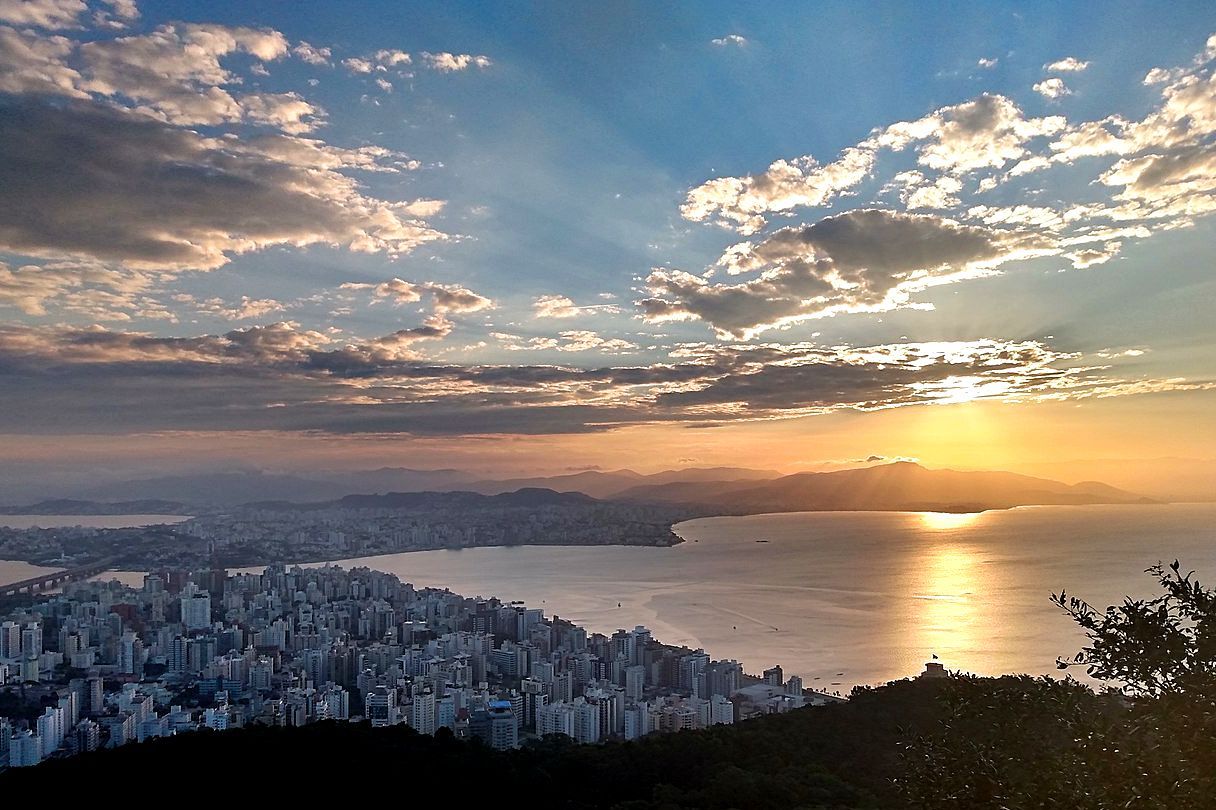 Vista aérea da cidade cercada pelo mar durante um pôr do sol e nuvens no céu.