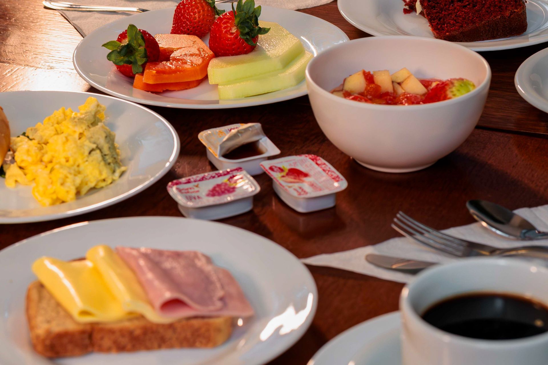 Mesa de café da manhã com frutas, ovos mexidos, pão, frios e copo com suco