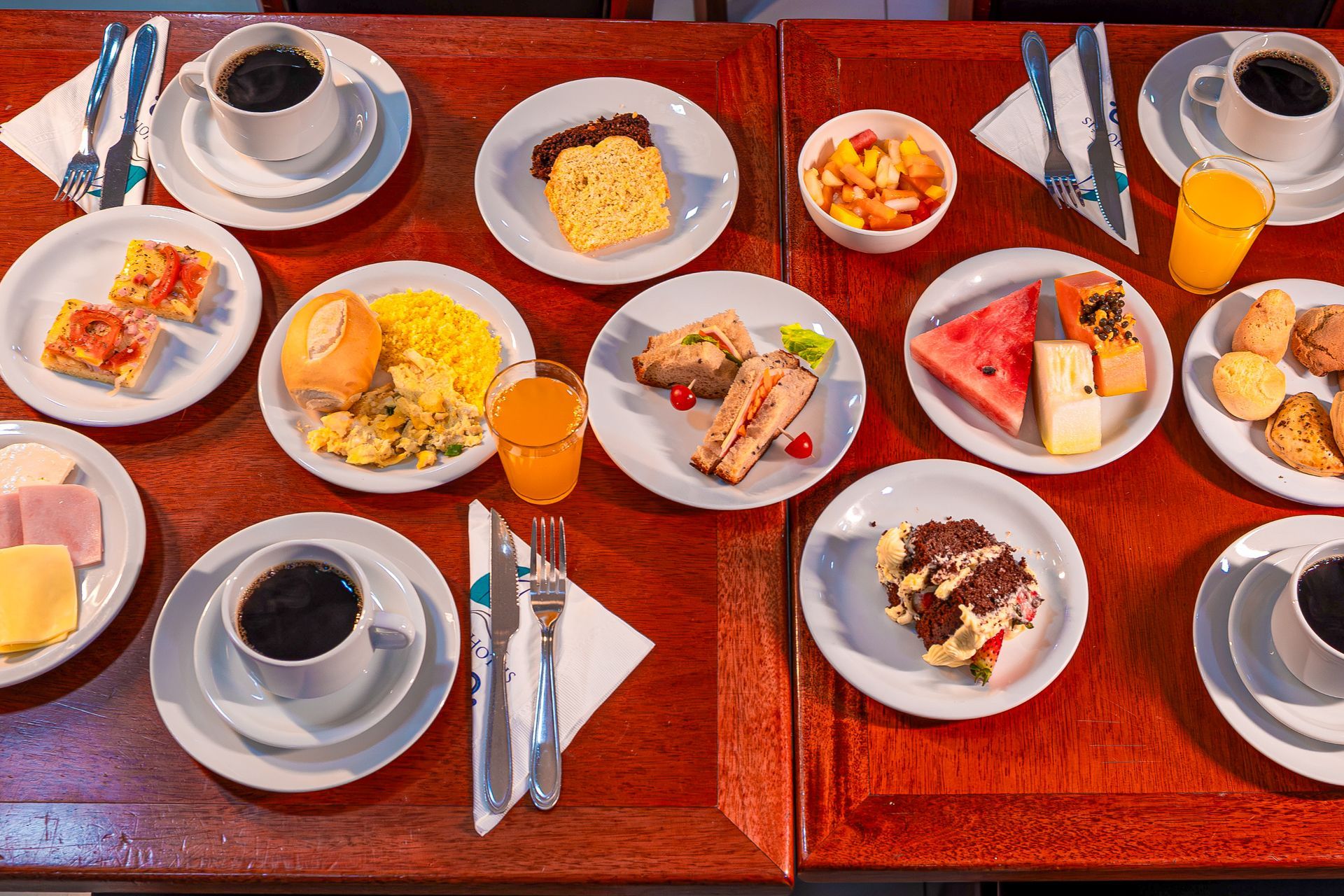 Mesa de café da manhã com frutas, pães, bolos, frios, sucos e café
