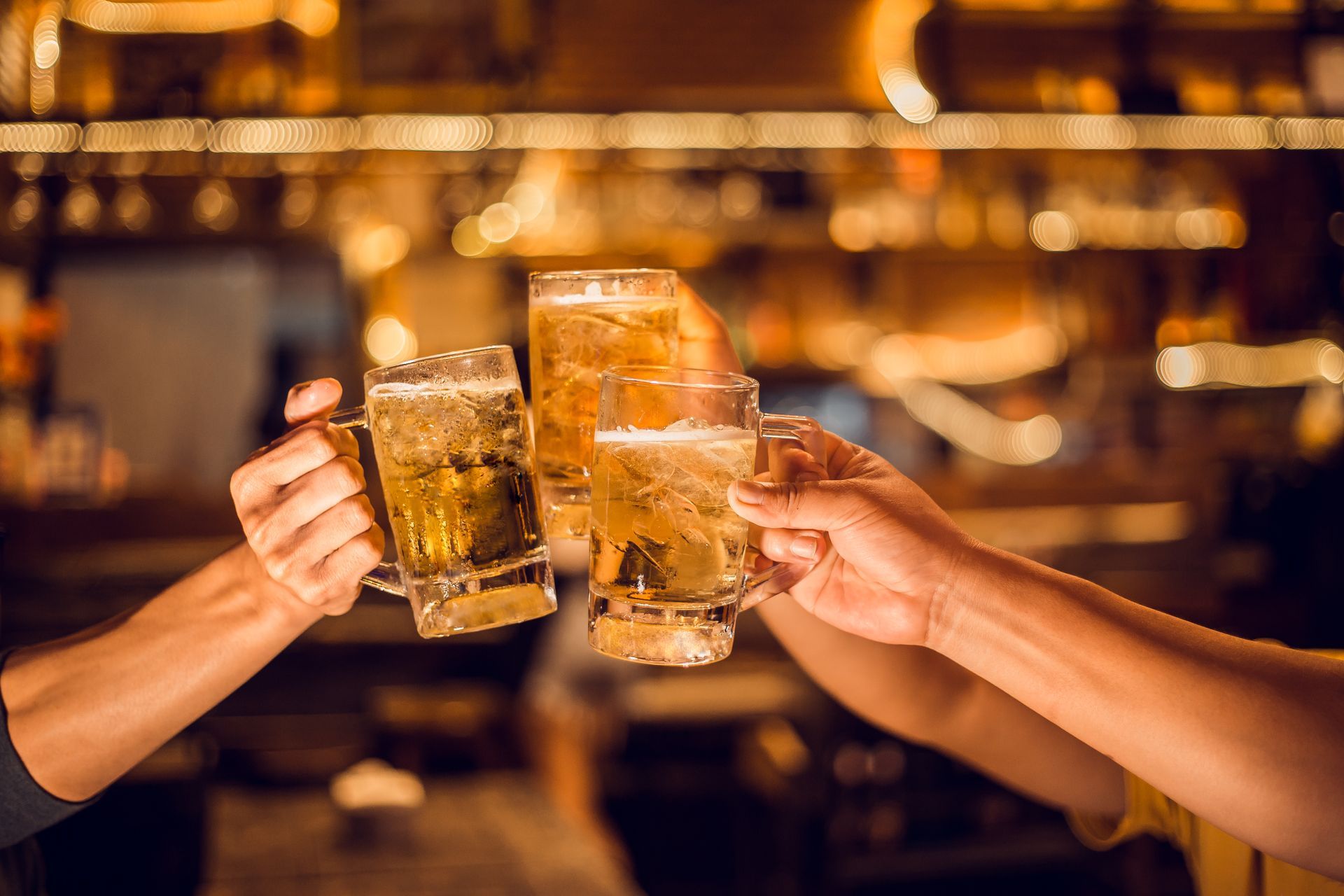 Três pessoas brindando com canecas de cerveja em um bar iluminado