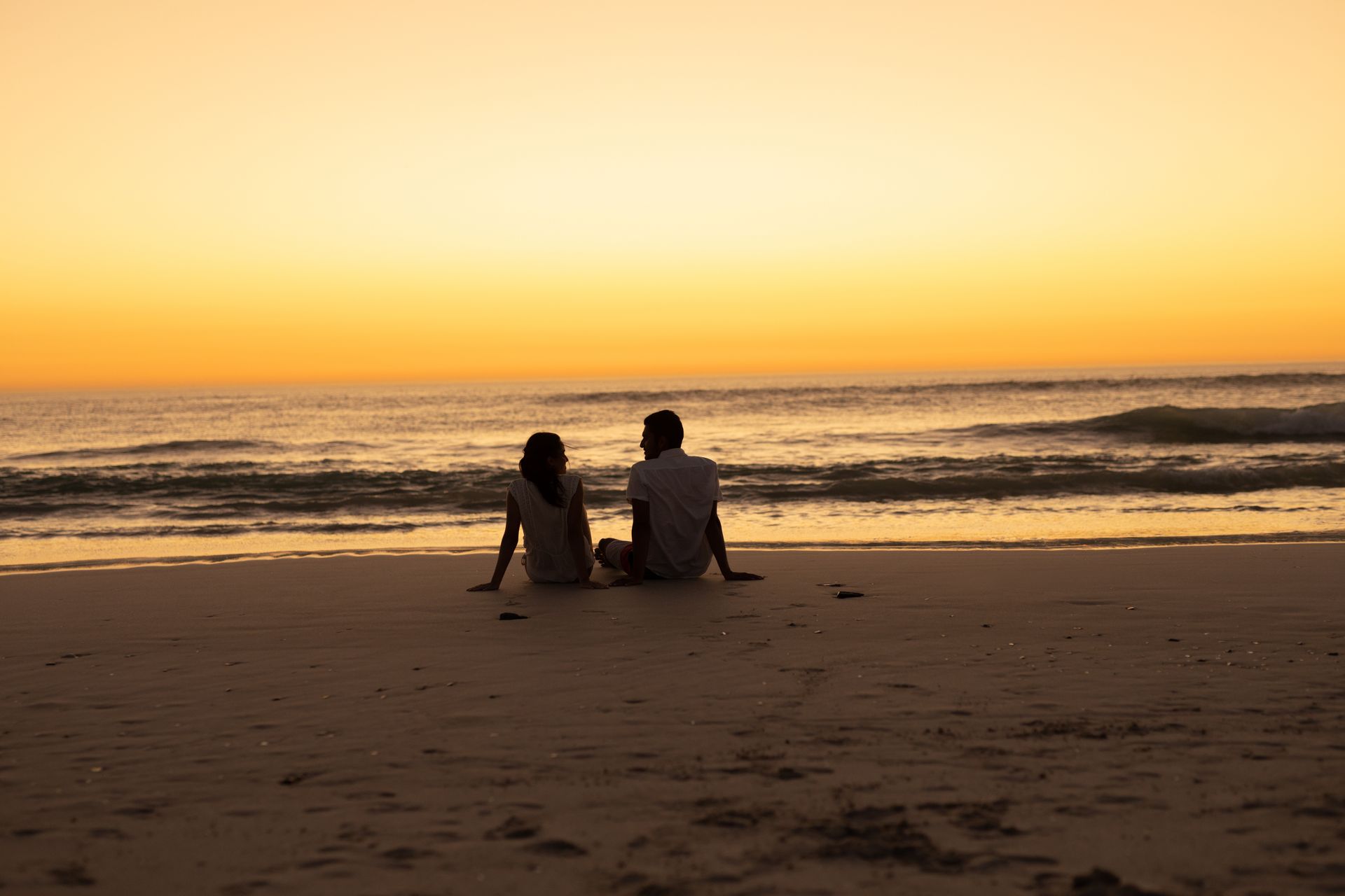 casal caminha de mãos dadas pela praia ao entardecer.