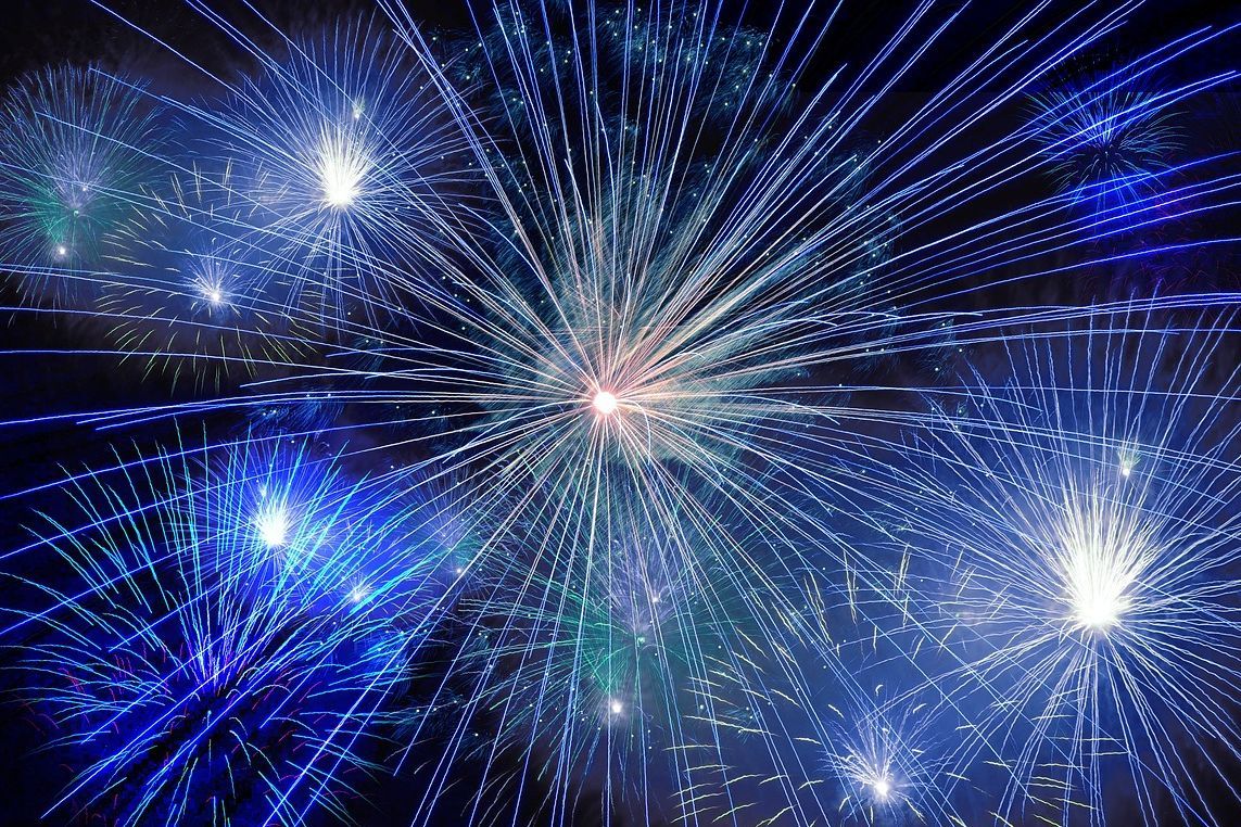 Fogos de artifício azuis e brancos explodem no céu noturno.