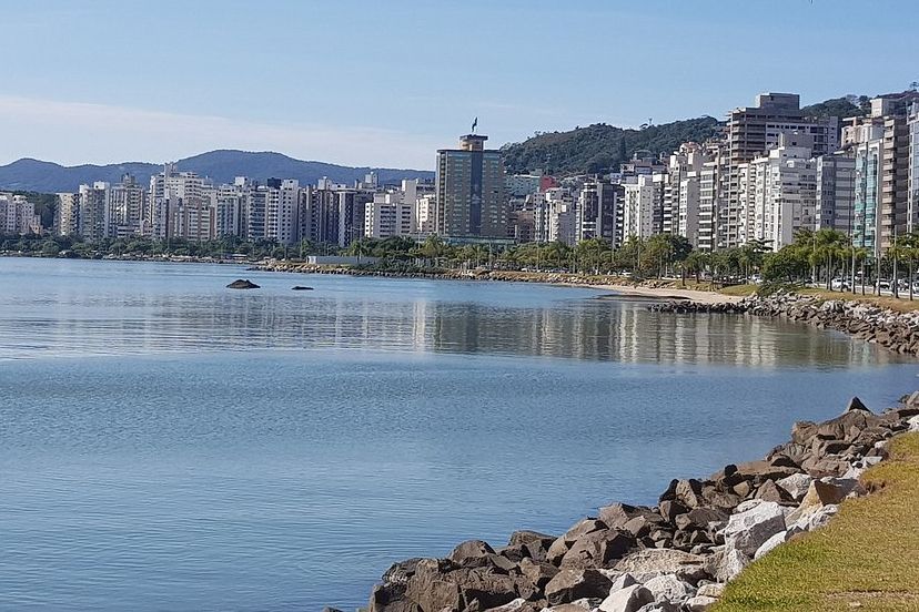 orla urbana com prédios altos se estende ao longo de águas calmas e rochas na beira-mar.