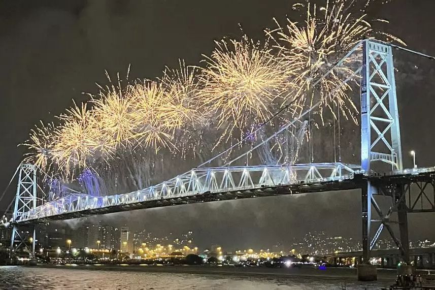 Fogos de artifício explodem à noite sobre uma ponte iluminada.