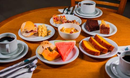 Mesa de café da manhã com pão, frutas, café e bolos variados