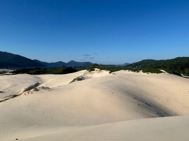 Vista das dunas da Dunas da Joaquina com areia branca e montanhas ao fundo em Florianópolis.