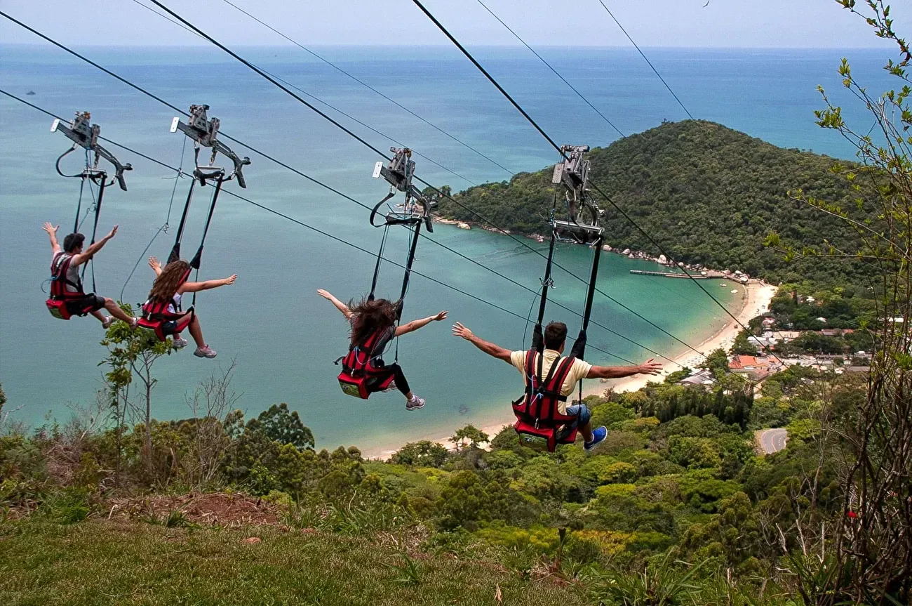 Pessoas descendo a tirolesa do Unipraias, com vista para a Praia de Laranjeiras.