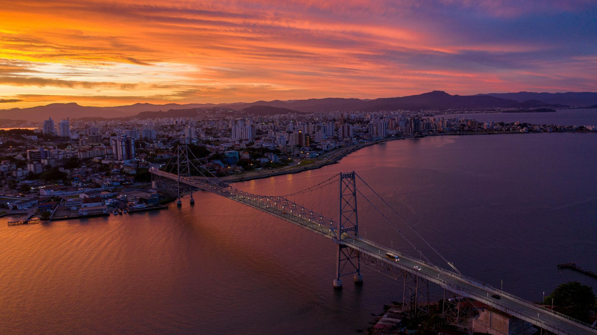 Ponte Hercílio Luz ao entardecer com a cidade de Florianópolis ao fundo.