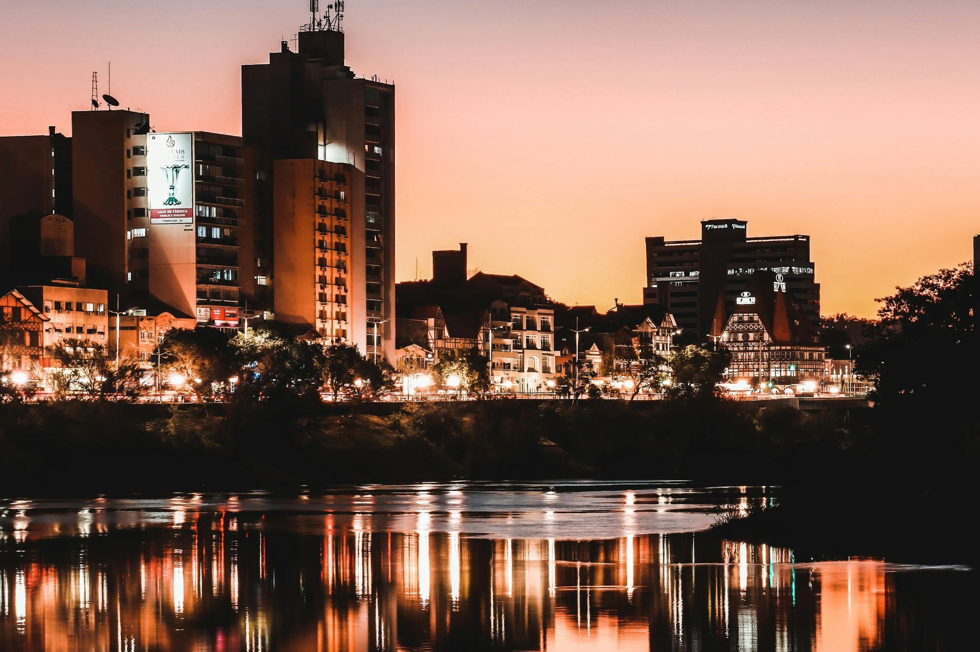Cidade iluminada ao entardecer refletida nas águas do rio.