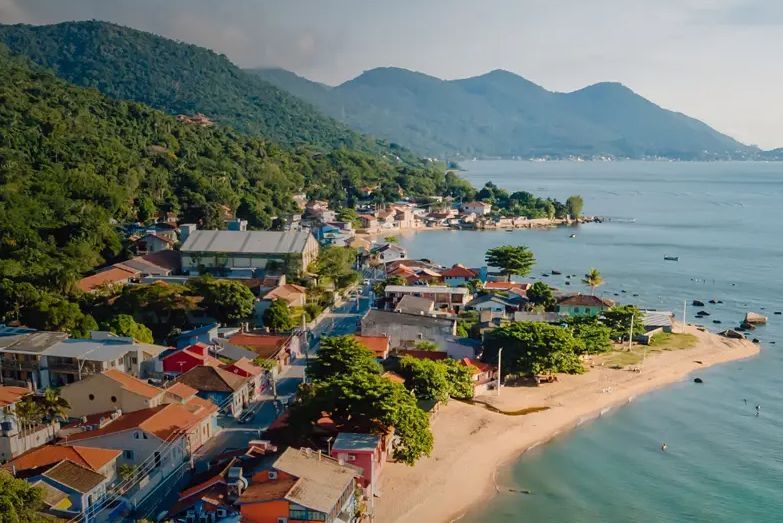 Vilarejo costeiro com casas coloridas entre o mar e montanhas cobertas de mata verde.