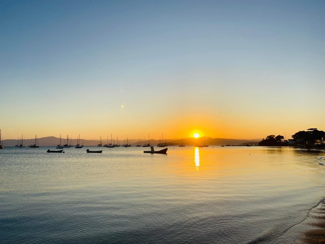 barcos descansam sobre as águas calmas do mar enquanto o sol se põe no horizonte.