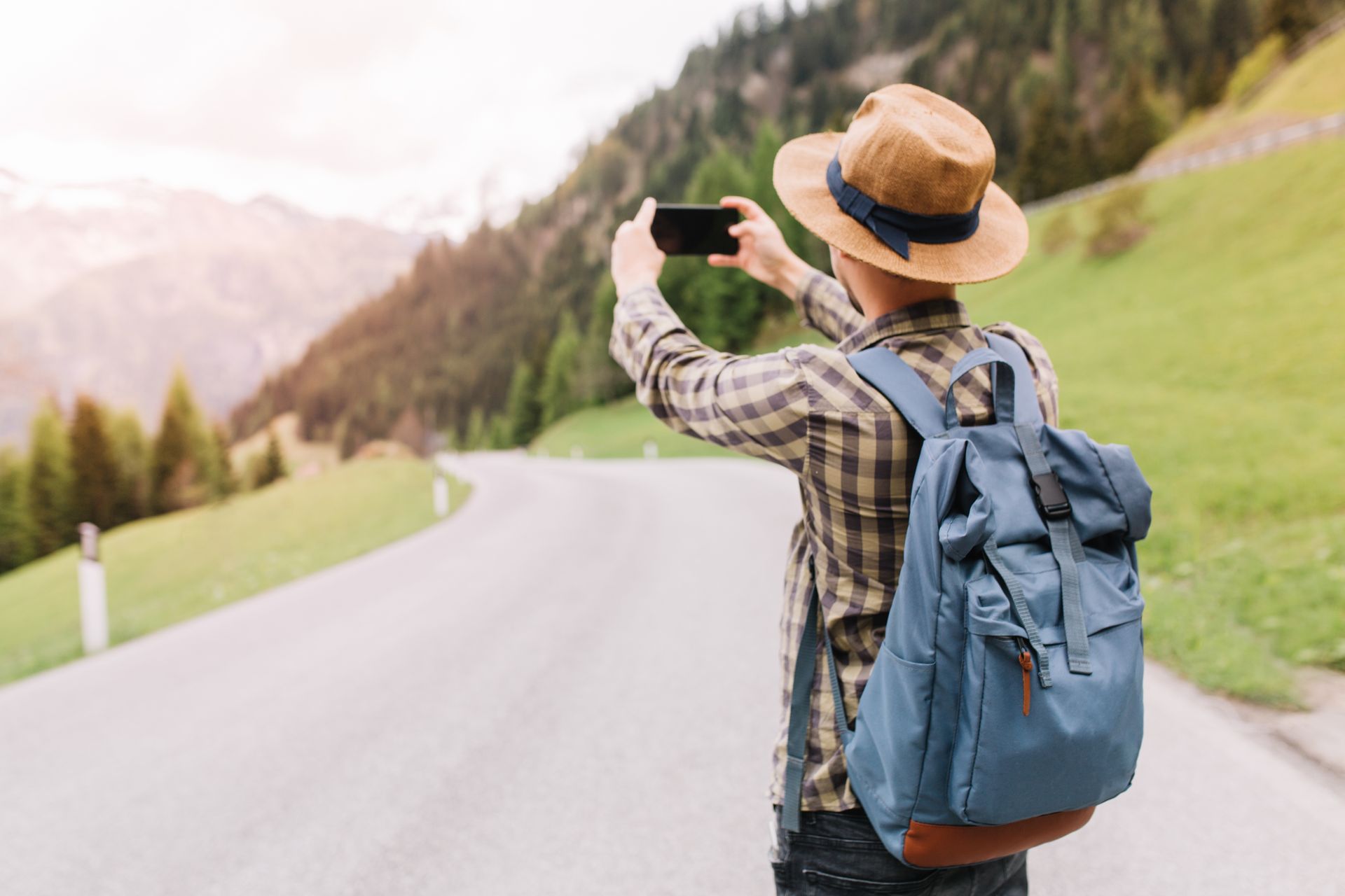 Turista tira foto em estrada cercada por montanhas.

