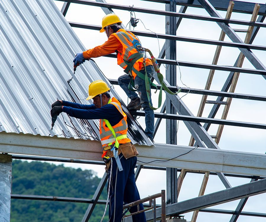 Two roofing installers are working to install metal roofing on a building's roof.