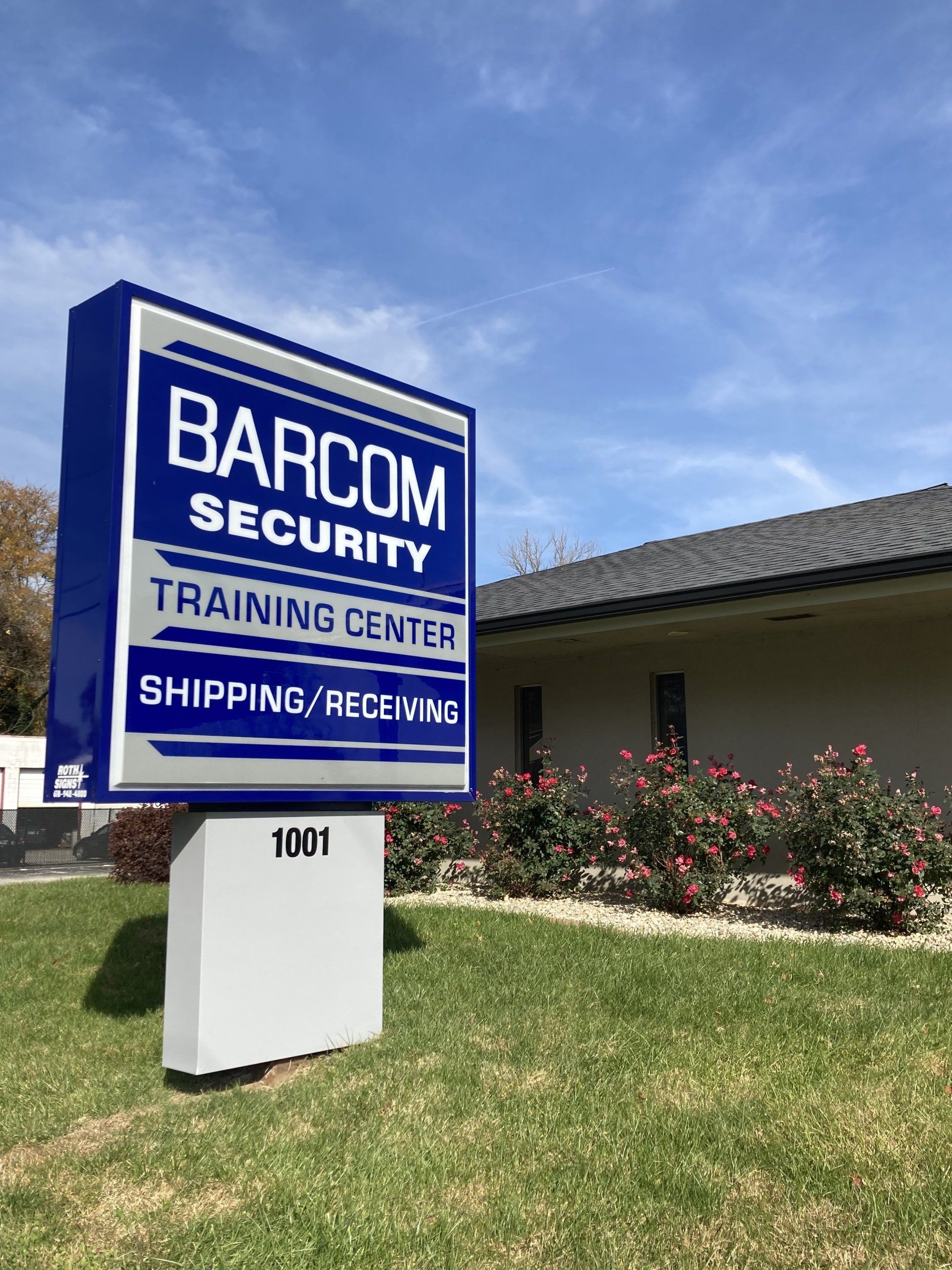 A blue and white sign for barcom security training center is in front of a building.